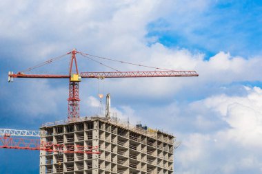 Mavi gökyüzüne karşı modern çok katlı bir konut kompleksinin yapımında birkaç kırmızı turna kullanıldı. Müteahhit mesleği olan insanlar için konsept iş.