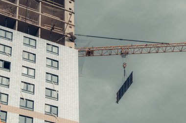 İnşaat aşamasında bir vinç, bir eve ve gri gökyüzüne doğru çekiliyor. Düşük gelirli genç aileler için endüstri konsepti. İpotek, iş, gayrimenkul kredisi.