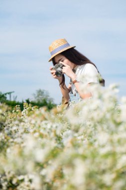 Asya hipster sevimli genç kız beyaz çiçek bahçesi kamera ile,
