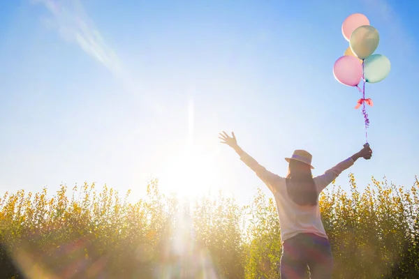 Chica corriendo en el campo de flores amarillas con globos al sol — Foto de Stock