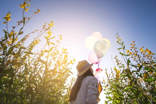 Chica corriendo en el campo de flores amarillas con globos al sol — Foto de Stock