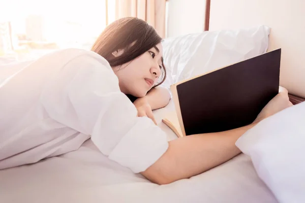 Wanita membaca buku dan minum kopi di tempat tidur selama pagi hari — Stok Foto