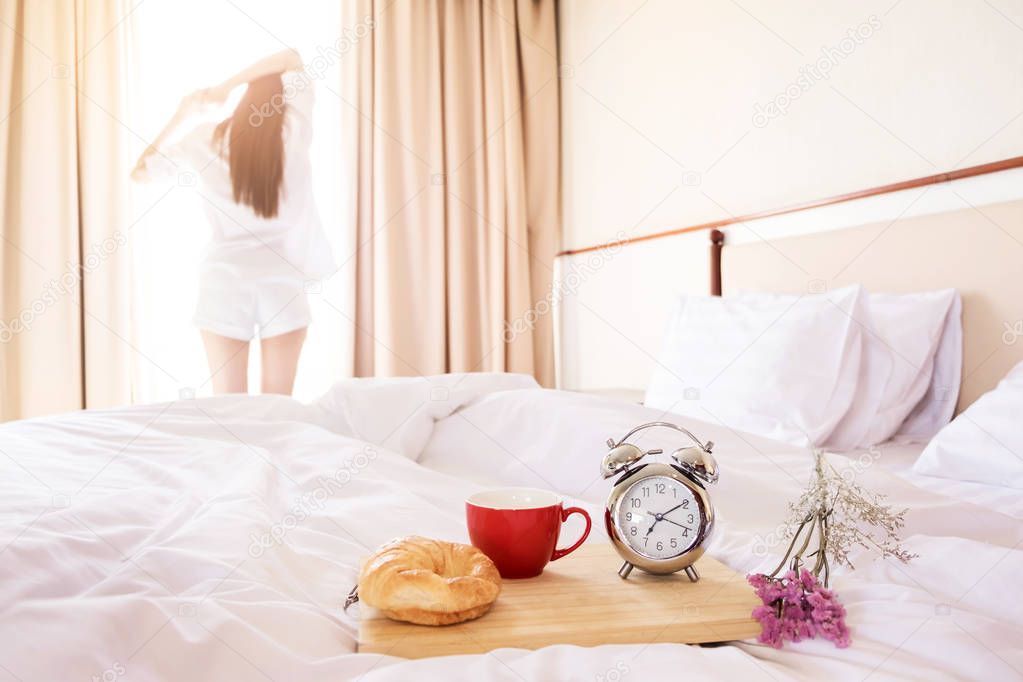 Woman stretched in bed room after the alarm clock and bread in t
