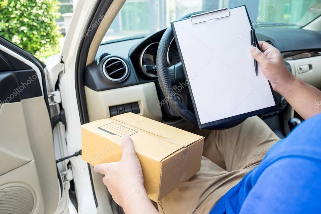 Delivery man with cardboard box checking document list In van an