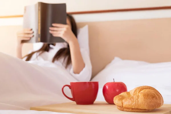 Wanita membaca buku dan minum kopi di tempat tidur selama pagi hari — Stok Foto