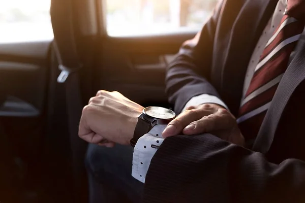 Handsome businessman looking on wrist watch in car — Stock Photo, Image