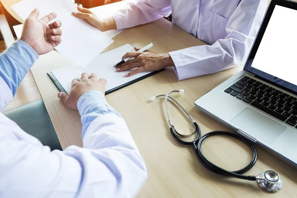 Doctors sitting at table and pointing to clipboard — Stock Photo, Image