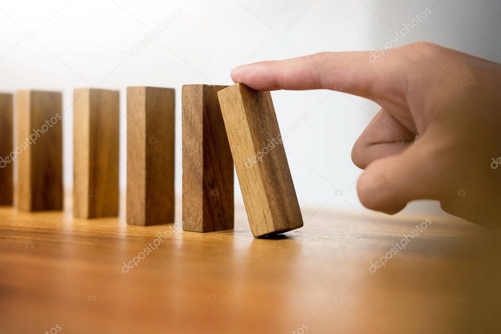 Hand of business man pushing dominoes for start on wooden backgr