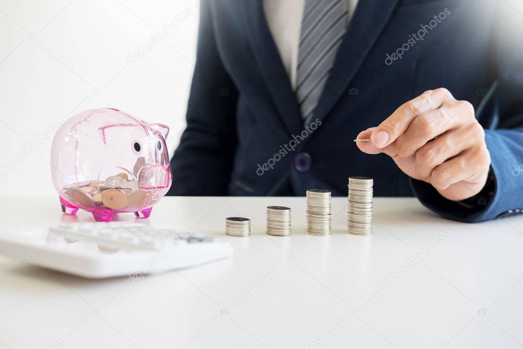 Close up of Businessman putting coin into small piggy bank , The