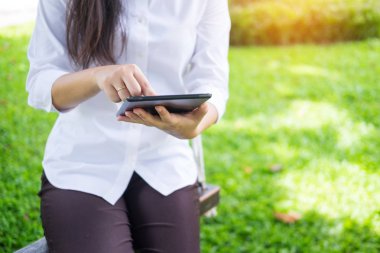 kadın bahçede bir şezlong üzerinde yatarken çalışmak için tablet kullanır.