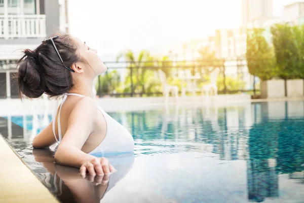 Mujer irreconocible en sombrero grande disfrutando de relajarse en la piscina en la villa de lujo, viajar cerca del mar y la playa en la puesta de sol . — Foto de Stock