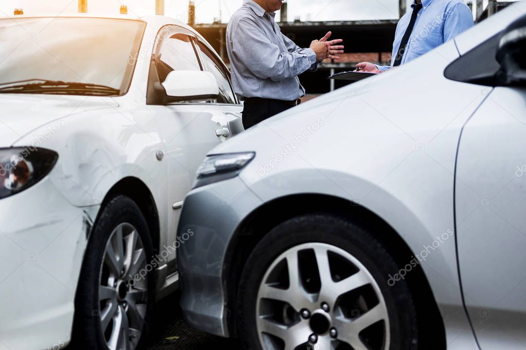 Insurance agent writing on clipboard while examining car after a