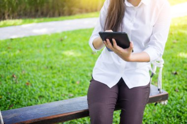 kadın bahçede bir şezlong üzerinde yatarken çalışmak için tablet kullanır.