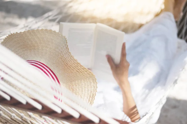 Νεαρή κυρία διαβάζει ένα βιβλίο σε αιώρα στην τροπική αμμώδη παραλία. — Φωτογραφία Αρχείου