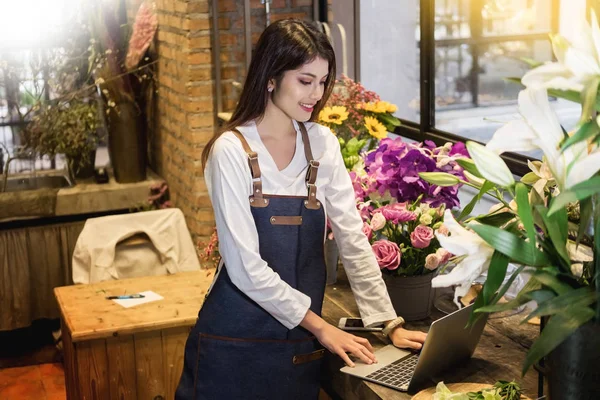 Women florist looking laptop got order at counter of her flower shop, occupation working concept