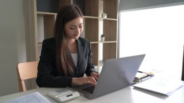 Kendine güvenen Asyalı iş kadınlarının dizüstü bilgisayarında yeni başlatılan proje ve iş yerindeki belgelerle birlikte çalıştıkları 4k video..