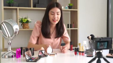 Ünlü blogcunun 4K videosu. Neşeli kadın vlogger makyaj dersleri için video kaydederken kozmetik ürünleri gösteriyor. iş yerinde.