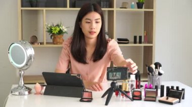 Ünlü blogcunun 4K videosu. Neşeli kadın vlogger makyaj dersleri için video kaydederken kozmetik ürünleri gösteriyor. iş yerinde.