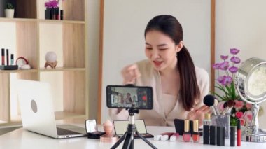 Ünlü blogcunun 4K videosu. Neşeli kadın vlogger makyaj dersleri için video kaydederken kozmetik ürünleri gösteriyor. iş yerinde.