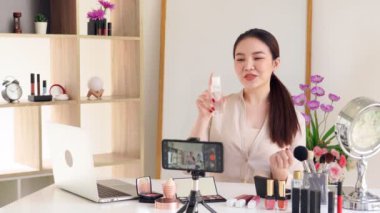 Ünlü blogcunun 4K videosu. Neşeli kadın vlogger makyaj dersleri için video kaydederken kozmetik ürünleri gösteriyor. iş yerinde.