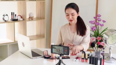 Ünlü blogcunun 4K videosu. Neşeli kadın vlogger makyaj dersleri için video kaydederken kozmetik ürünleri gösteriyor. iş yerinde.