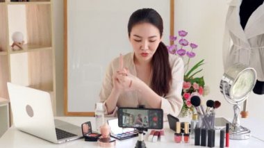 Ünlü blogcunun 4K videosu. Neşeli kadın vlogger makyaj dersleri için video kaydederken kozmetik ürünleri gösteriyor. iş yerinde.