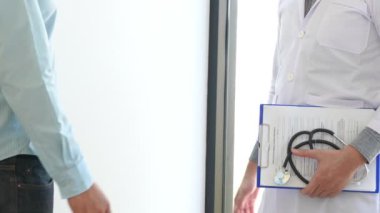 Doktor 'un muayenehanede gözlük, steteskop ve laboratuvar önlüğü takıp hastayla el sıkıştığı 4K video.