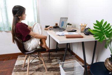 Attractive young beautiful asian woman working with laptop and document while sitting at the indoors living room office as a freelancer, e-coaching working, remotely or work from home concept clipart