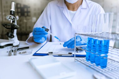 Laboratuvarda beyaz önlükle araştırma yapan bilim adamları eldivenleri analiz ediyor, test tüpleri örneklerine bakıyor, biyoteknoloji kavramına bakıyor..