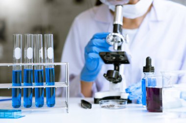 Genç Asyalı bilim adamı mikroskopla inceleyerek adli tıp laboratuarındaki bir deney örneğini analiz ediyor.