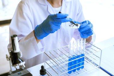 Laboratuvarda beyaz önlükle araştırma yapan bilim adamları eldivenleri analiz ediyor, test tüpleri örneklerine bakıyor, biyoteknoloji kavramına bakıyor..