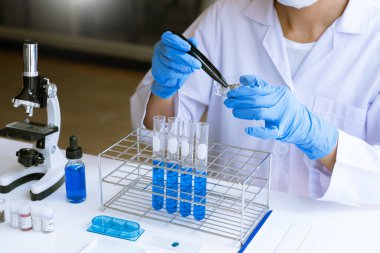 Laboratuvarda beyaz önlükle araştırma yapan bilim adamları eldivenleri analiz ediyor, test tüpleri örneklerine bakıyor, biyoteknoloji kavramına bakıyor..