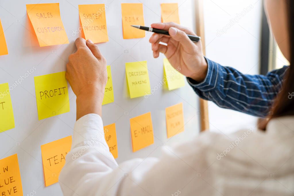 Business people arranging sticky notes commenting and brainstorming on work priorities colleague in a modern co-working space