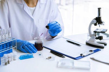 Laboratuvarda beyaz önlükle araştırma yapan bilim adamları eldivenleri analiz ediyor, test tüpleri örneklerine bakıyor, biyoteknoloji kavramına bakıyor..