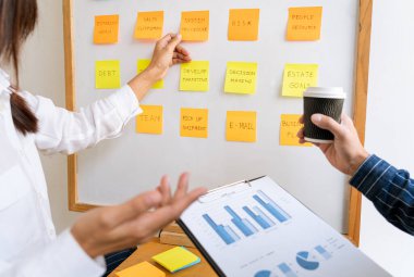 Yapışkan notlar yazan genç iş adamları, modern bir çalışma alanındaki meslektaşlarına yaratıcı beyin fırtınalarını hatırlatıyor.