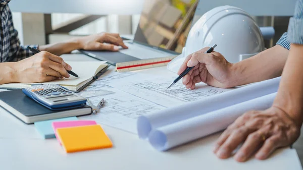 エンジニアハンド図面計画ブループリント現代的なオフィスのテーブルで設計図の建築計画の上のフロアプランを議論する建築機器と — ストック写真
