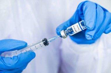 Doktor, bilim adamı, mavi eldivenli bir araştırmacı ya da koruyucu giysi giymiş. İnsan klinik enjeksiyon deneylerine hazırlanıyor. Cvid-19 Coronavirus aşısı biyolojik tehlike kavramı.