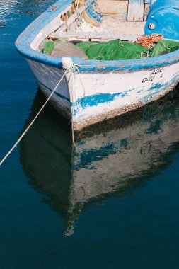 Pequea barca de  pesca de madera azul y verde atada en un pantaln con cuerda marina
