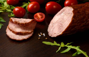 Tütsülenmiş sosis, jambon ile kırmızı domates ve karanlık bir plaka üzerinde otlar