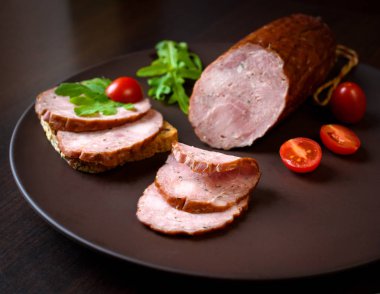 Tütsülenmiş sosis, jambon ile kırmızı domates ve karanlık bir plaka üzerinde otlar