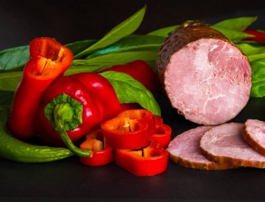 Tütsülenmiş sosis, kırmızı ve yeşil biber ve karanlık bir arka plan üzerinde otlar ile jambon