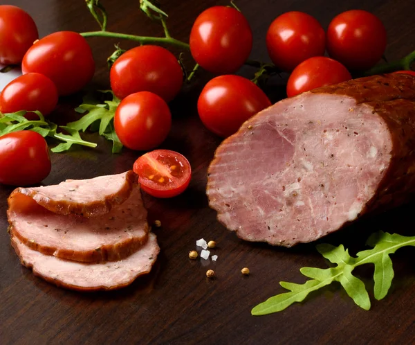 Salsicha defumada, presunto com tomates vermelhos e ervas em um prato escuro — Fotografia de Stock