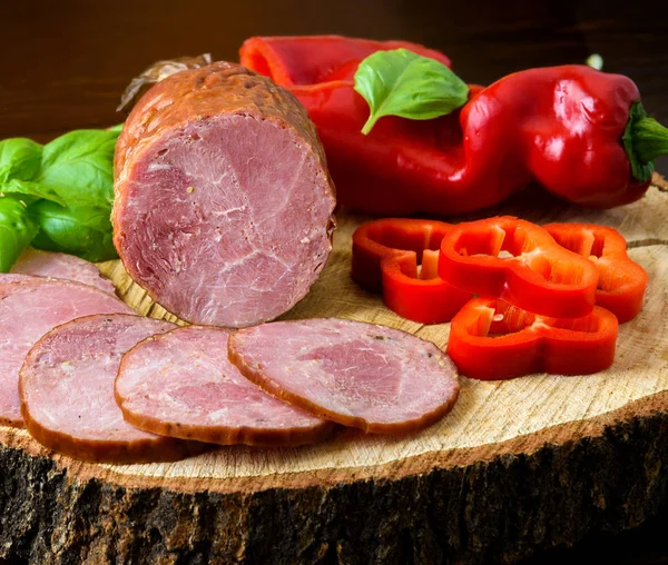 Smoked sausage, ham with red and green peppers and herbs on a dark background — Stock Photo, Image