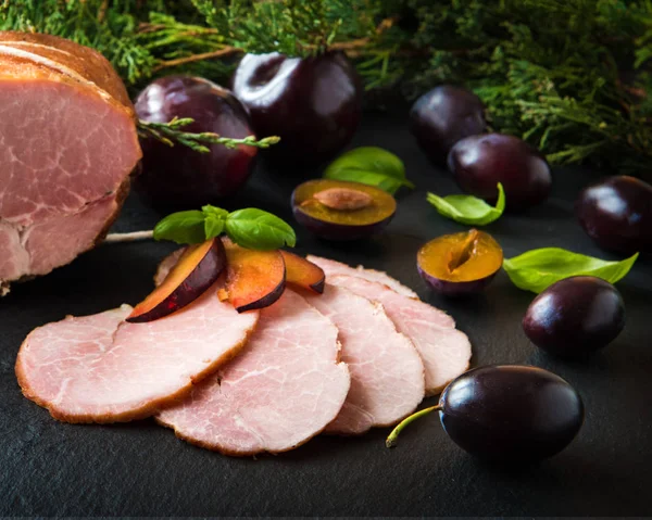 Smoked ham with herbs, fruits (plumps) on black background — Stock Photo, Image