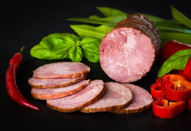 Tütsülenmiş sosis, kırmızı ve yeşil biber ve karanlık bir arka plan üzerinde otlar ile jambon