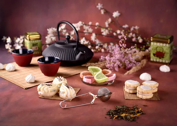 中国或日本茶壶 有杯子 蛋糕和深红色背景的花朵 — 图库照片