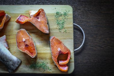 Ahşap bir tahtanın üzerinde taze kırmızı balık parçaları uzanıyor. Kuru otlarla birlikte pembe somon balığı.