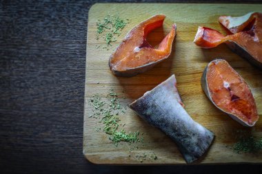 Küçük taze kırmızı balık parçaları pembe somon, kurutulmuş otlar ve baharatlarla ahşap bir kesme tahtasının üzerinde uzanıyor.