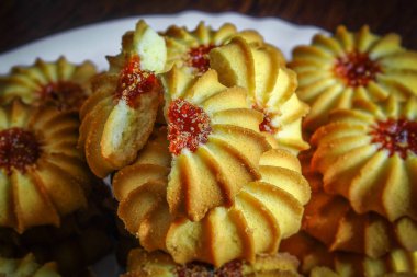 Masanın üzerinde beyaz bir tabakta taze tatlı bisküviler ve reçel var.