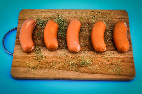 In the horizontal photo, a blue background, sausages on a wooden cutting Board